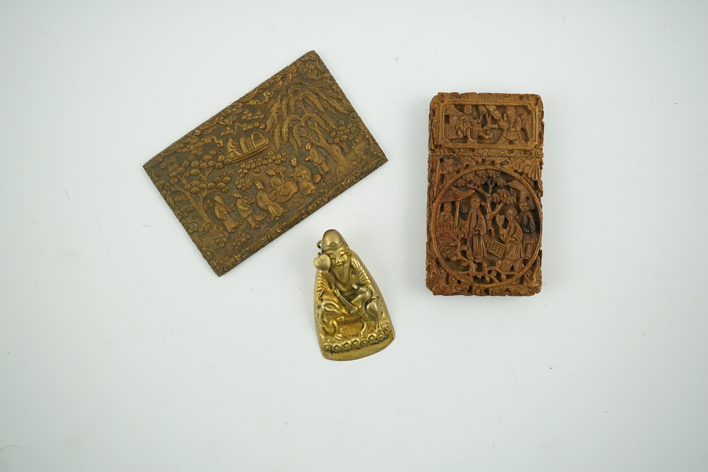 A Chinese carved sandalwood card case, a bronze relief cast and chased plaque and a gilt metal Shou Lao pendant, card case 7.5cm high. Condition - good